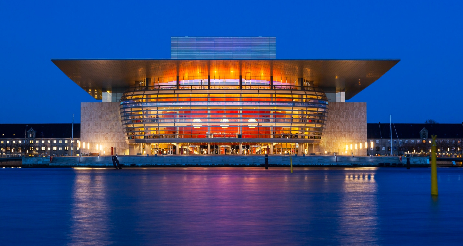 Copenhagen Opera House illuminated at night with reflections on the water. Join us in 2025 for Scandinavia Opera tour.